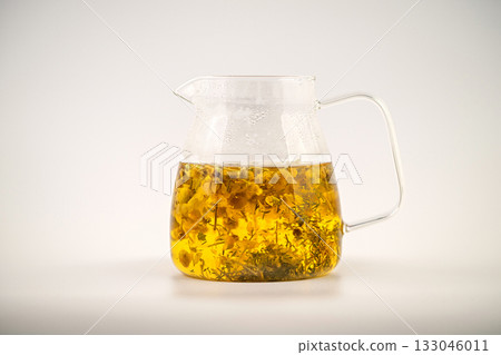 A glass of Chamomile tea with flowers floating in it. The tea is yellow and the flowers are white A glass of Chamomile tea with flowers floating in it. The tea is yellow and the flowers are white 133046011