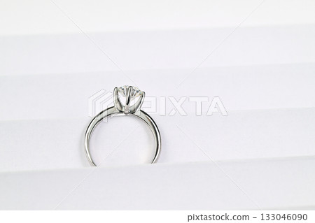 A silver ring with a diamond in the center sits on a white surface 133046090