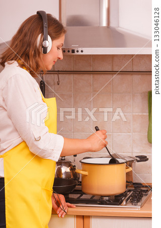 Housewife with earphones in kitchen Housewife with earphones in kitchen 133046128