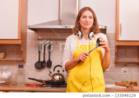 Housewife with earphones in kitchen Housewife with earphones in kitchen 133046129