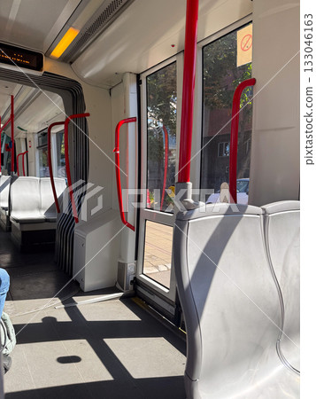 Modern tram interior with red handrails and sunlight. Transportation, urban design, and everyday mobility. 133046163