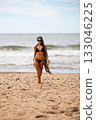 A stylish model gracefully strutting along the soft sandy beach, wearing a chic black bikini and trendy sunglasses 133046225