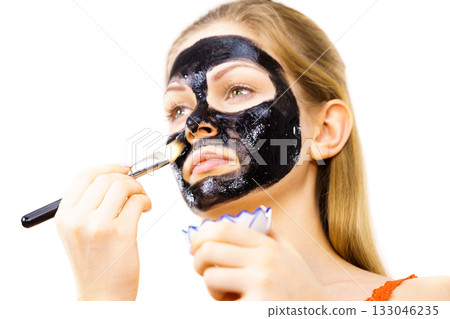 Woman applying black mud mask to face Woman applying black mud mask to face 133046235