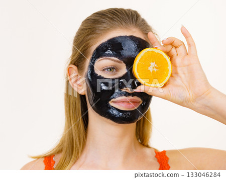 Girl black carbo mask on face holds orange fruit Girl black carbo mask on face holds orange fruit 133046284