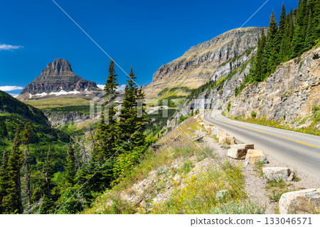 Scenic view of the winding Going-to-the-Sun Road in Glacier National Park, Montana. The iconic Clements Mountain rises in the distance under a clear blue sky. Represents travel and nature Scenic view of the winding Going-to-the-Sun Road in Glacier National Park, Montana. The iconic Clements Mountain rises in the distance under a clear blue sky. Represents travel and nature 133046571