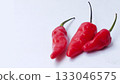 A bunch of bright red chilies with green stems arranged on a white background 133046575