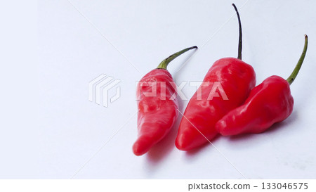 A bunch of bright red chilies with green stems arranged on a white background 133046575