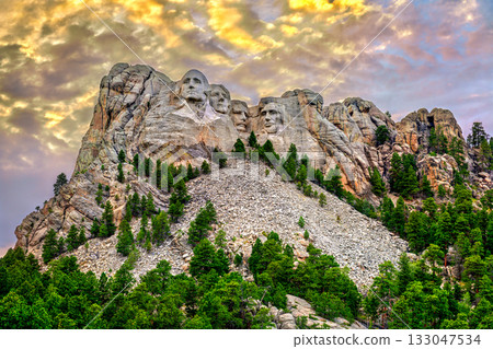 Mount Rushmore National Memorial in South Dakota. The granite carving of four presidents is lit under a dramatic, colorful cloudy sky at sunset 133047534