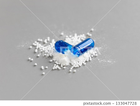 Opened Blue capsule to show white granules and powder on grey closeup. Medicine and Healthcare Opened Blue capsule to show white granules and powder on grey closeup. Medicine and Healthcare 133047728