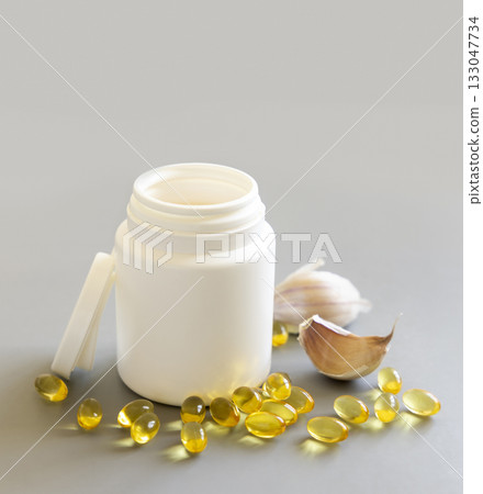 Bottle and yellow garlic oil capsules near cloves on a grey close up, mockup. Dietary supplement 133047734