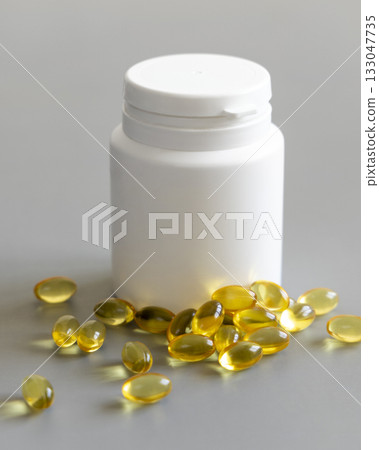 Yellow softgels (gelatin capsules) and bottle on a grey close up, mockup. Omega 3 Fish oil or garlic oil 133047735