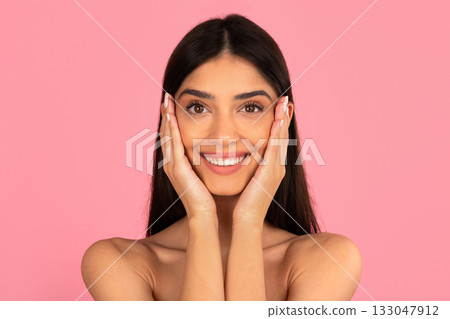 Happy young woman smiling with hands on cheeks against pink background 133047912