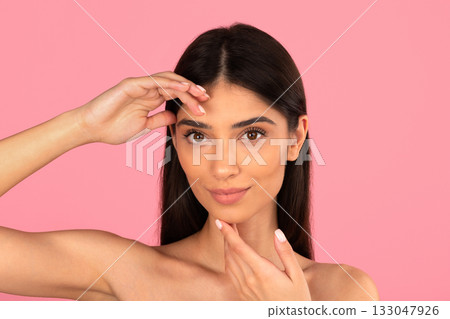 Confident young woman touching forehead and chin while looking at camera Confident young woman touching forehead and chin while looking at camera 133047926