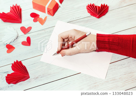 girl writes a love letter on a bright table with red symbols of love and a gift girl writes a love letter on a bright table with red symbols of love and a gift 133048023