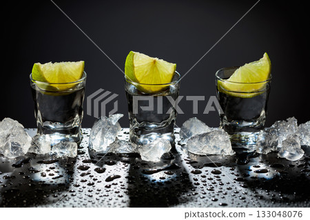 Tequila shots with lime slices on a wet black table. 133048076