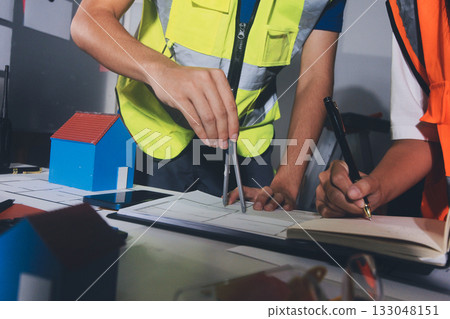 Closeup of team of industrial engineers meeting analyze machinery blueprints consult project on table in manufacturing factory. Working in manufacturing plant or production plant. Closeup of team of industrial engineers meeting analyze machinery blueprints consult project on table in manufacturing factory. Working in manufacturing plant or production plant. 133048151