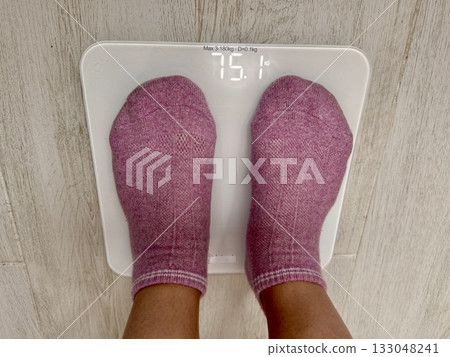 A young girl stands on an electronic floor scale to measure excess weight at home 133048241