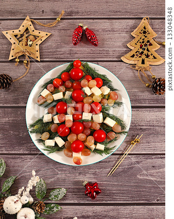 Christmas and New Year's dishes, traditional holiday salad in the form of a live edible Christmas tree with feta cheese, olives, tomatoes and grapes, fir branches and decorations, food design idea Christmas and New Year's dishes, traditional holiday salad in the form of a live edible Christmas tree with feta cheese, olives, tomatoes and grapes, fir branches and decorations, food design idea 133048348