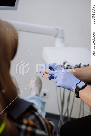 Dentist explaining treatment with 3D dental model to patient in chair, clinical consultation 133048359