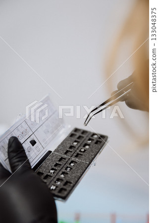 Orthodontic bracket kit with placement chart and tweezers, gloved hands, clinic closeup 133048375