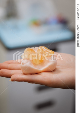 Transparent implant surgical guide on dental jaw model in clinician hand, clinic closeup 133048384