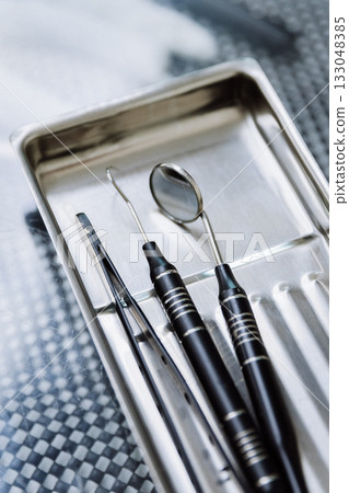Dental mirror, explorer and tweezers on sterile metal tray, clinic closeup Dental mirror, explorer and tweezers on sterile metal tray, clinic closeup 133048385