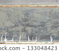 A fragment of an old building wall with a gray, worn surface, streaks of white paint and rusty metal stripes, part of the exterior of an abandoned building as a rough, grunge background 133048423