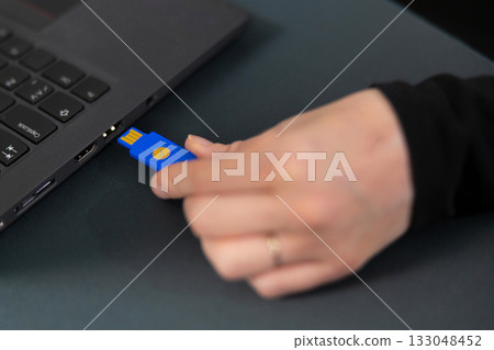 Female IT security technician in a tech office connects blue USB drive to a laptop 133048452