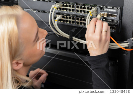Female IT technician in a data center installing and securing network equipment in a server rack 133048458