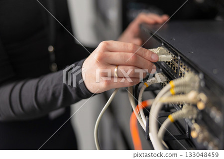 Woman IT technician connects network cables to server rack in data center for maintenance 133048459