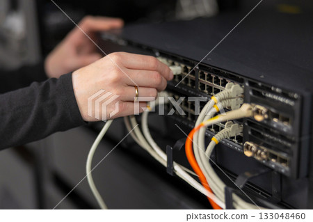 Female IT technician in a datacenter connecting and configuring network switches with cables 133048460