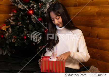 The woman is opening a Christmas present near the Christmas tree The woman is opening a Christmas present near the Christmas tree 133048594