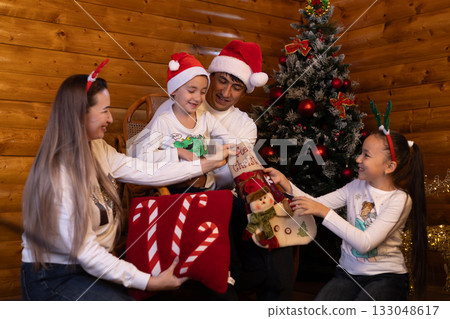 Children joyfully unwrap gifts around a twinkling Christmas tree Children joyfully unwrap gifts around a twinkling Christmas tree 133048617
