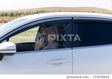 Man is talking on a mobile phone inside a white car Man is talking on a mobile phone inside a white car 133048694