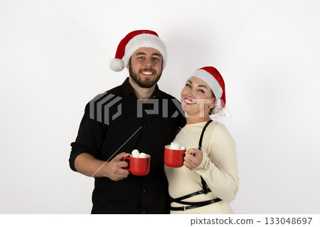 The couple is enjoying hot cocoa while wearing Santa hats for the Christmas The couple is enjoying hot cocoa while wearing Santa hats for the Christmas 133048697