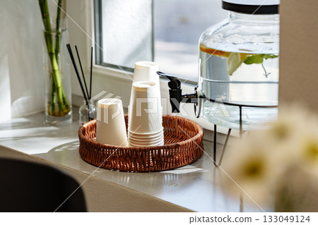 Coffee cups and water dispenser on a bright windowsill in a cozy cafe setting 133049124
