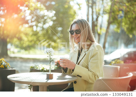 Woman enjoying coffee outdoors on a sunny day in a lively urban setting Woman enjoying coffee outdoors on a sunny day in a lively urban setting 133049131