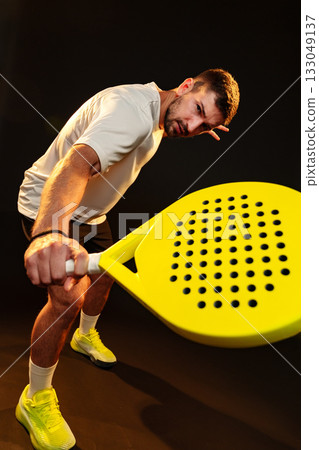 Man plays pickleball with a bright yellow paddle in a dark indoor setting Man plays pickleball with a bright yellow paddle in a dark indoor setting 133049137