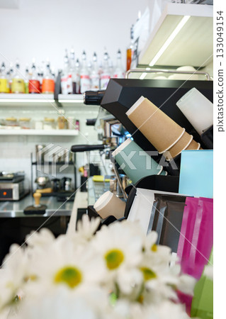 Coffee shop equipment and colorful cups on display with flowers in the foreground 133049154