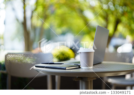 Laptop and coffee cup on table outdoors in a sunny urban setting Laptop and coffee cup on table outdoors in a sunny urban setting 133049171