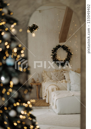 Cozy bedroom with Christmas wreath and blurred decorated tree with warm lights Cozy bedroom with Christmas wreath and blurred decorated tree with warm lights 133049402
