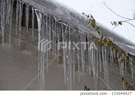 Cold winter, ice formation. Big icicles hang from roof of house 133049427