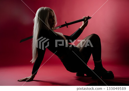Stylish warrior with sword posing against a dramatic red background in an urban setting 133049589