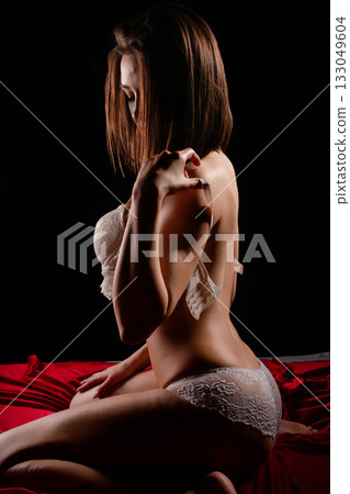 Model poses gracefully on a red bedspread in soft light capturing elegance and beauty 133049604