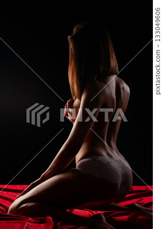 Model posing on a red fabric backdrop in a dimly lit studio setting 133049606