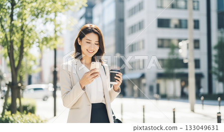 一位女商人一邊操作智慧型手機，一邊手拿一杯咖啡。 133049631