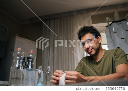 Home gardener wearing safety glasses carefully measuring and preparing fertilizer for vertical hydroponic tower garden, ensuring optimal plant growth and nutrient supply. Concept of indoor farming. Home gardener wearing safety glasses carefully measuring and preparing fertilizer for vertical hydroponic tower garden, ensuring optimal plant growth and nutrient supply. Concept of indoor farming. 133049750