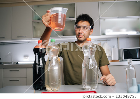 Chemist wearing safety glasses holding beaker with liquid fertilizer, prepared from various chemicals in laboratory, emphasizing fertilizer preparation for agriculture and science. Chemist wearing safety glasses holding beaker with liquid fertilizer, prepared from various chemicals in laboratory, emphasizing fertilizer preparation for agriculture and science. 133049755