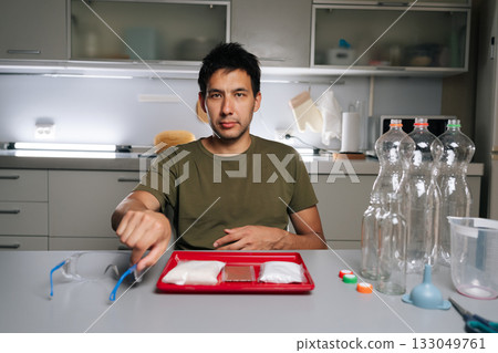 Portrait of plant researcher male wearing safety glasses while preparing fertilizer for vertical hydroponic tower garden, ensuring safe handling of chemicals in kitchen. Concept of urban farming. Portrait of plant researcher male wearing safety glasses while preparing fertilizer for vertical hydroponic tower garden, ensuring safe handling of chemicals in kitchen. Concept of urban farming. 133049761