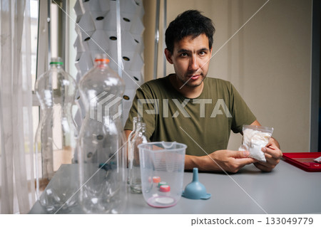 Portrait of gardener male sitting at table preparing to mixing fertilizer from bottles for innovative vertical garden setup, emphasizing eco-friendly urban agriculture. Concept of indoor farming. Portrait of gardener male sitting at table preparing to mixing fertilizer from bottles for innovative vertical garden setup, emphasizing eco-friendly urban agriculture. Concept of indoor farming. 133049779